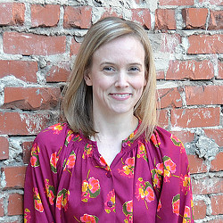 A woman smiling in front of a brick wall.